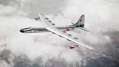 Das Foto zeigt die Convair NB-36H der United States Air Force im Flug über einer geschlossenen Wolkendecke. Das großspannige Propellerflugzeug, eine modifizierte B‑36 für Nuklearforschungszwecke, ist in Schrägaufsicht mit deutlich erkennbaren Triebwerksgondeln und Leitwerk aufgenommen. Laut Dateiname stammt die Aufnahme aus dem Jahr 1955 und zeigt die Maschine im Verband mit einer Boeing B‑50 (USAF).