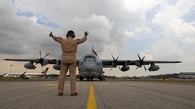Soldat weist KC-130J Super Hercules ein mit Airliner im Hintergrund