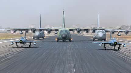 Mehrere Militärflugzeuge, darunter Transportflugzeuge und Kampfflugzeuge, rollen auf einer Start- und Landebahn.