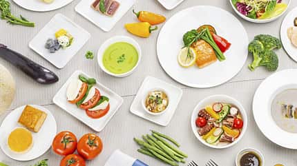 Eine Vielzahl von verschiedenen Gerichten und frischem Gemüse, kunstvoll auf einem Tisch arrangiert. Die Speisen sind auf weißen Tellern und Schalen angerichtet.