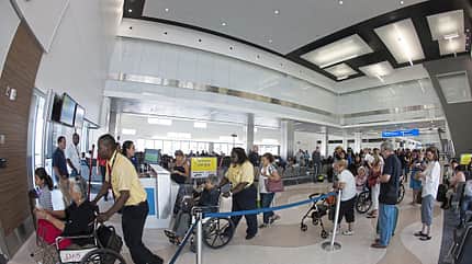 Menschen stehen in einer Warteschlange an einem Flughafengate. Einige Personen sitzen in Rollstühlen und werden von Mitarbeitern begleitet.