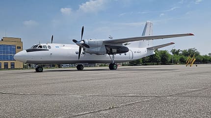 Flugzeug, Propellerflugzeug, Rollfeld, Flughafen, Luftfahrt Ein Propellerflugzeug steht auf dem Rollfeld eines Flughafens bei Tageslicht. Im Hintergrund sind ein Gebäude und einige Bäume zu sehen.