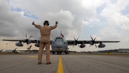 Soldat weist KC-130J Super Hercules ein mit Airliner im Hintergrund