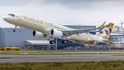 Ein Passagierflugzeug der Fluggesellschaft Etihad Airways startet von einer Landebahn, im Hintergrund sind Industriegebäude zu sehen.