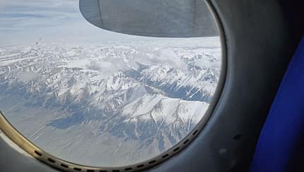 Blick aus einem Flugzeugfenster auf schneebedeckte Berge und Wolken.