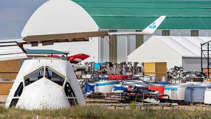 Flugzeugnase, Flugzeugfriedhof, Teruel, KLM, Flugzeugteile, Luftfahrt, Flugzeugwrack, Flugzeugdemontage, Juni 2021, Flugzeughangar Flugzeugnase und Flugzeugteile auf einem Flugzeugfriedhof in Teruel, Juni 2021. Im Hintergrund Hallen und weitere Flugzeugkomponenten, darunter ein KLM-Seitenleitwerk.