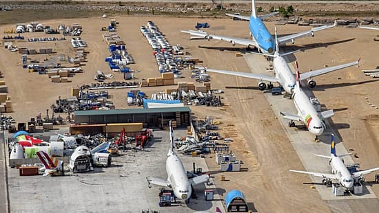 Luftaufnahme eines Flugzeugfriedhofs mit mehreren abgestellten und teilweise zerlegten Verkehrsflugzeugen in Teruel. Zu sehen sind Flugzeuge verschiedener Airlines, darunter KLM, TAP, Lufthansa und weitere, sowie zahlreiche Flugzeugteile und Komponenten auf dem Gelände.