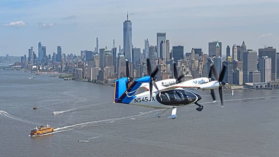 Das Foto zeigt das elektrische Lufttaxi von Joby Aviation im Flug über New York. Das eVTOL mit mehreren schwenkbaren Propellern trägt die Kennung N545JX und fliegt über dem Hudson River; im Hintergrund ist die Skyline von Manhattan mit dem One World Trade Center sichtbar. Laut Dateiname stammt die Aufnahme aus dem Jahr 2026.