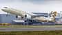 Ein Passagierflugzeug der Fluggesellschaft Etihad Airways startet von einer Landebahn, im Hintergrund sind Industriegebäude zu sehen.