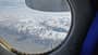 Blick aus einem Flugzeugfenster auf schneebedeckte Berge und Wolken.