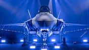 Eine F-35 auf einer Bühne wird mit blauem Licht angestrahlt.