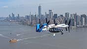 Das Foto zeigt das elektrische Lufttaxi von Joby Aviation im Flug über New York. Das eVTOL mit mehreren schwenkbaren Propellern trägt die Kennung N545JX und fliegt über dem Hudson River; im Hintergrund ist die Skyline von Manhattan mit dem One World Trade Center sichtbar. Laut Dateiname stammt die Aufnahme aus dem Jahr 2026.