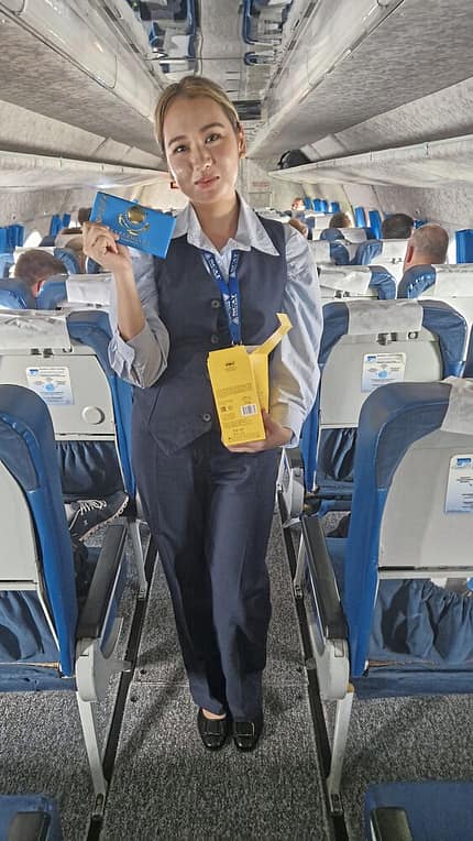 Flugbegleiterin, Flugzeug, Kabine, Schokolade, Passagiere, Luftfahrt Eine Flugbegleiterin steht im Gang eines Flugzeugs und hält eine Schokoladentafel sowie eine gelbe Verpackung in der Hand. Im Hintergrund sind Passagiere auf ihren Sitzen zu sehen.